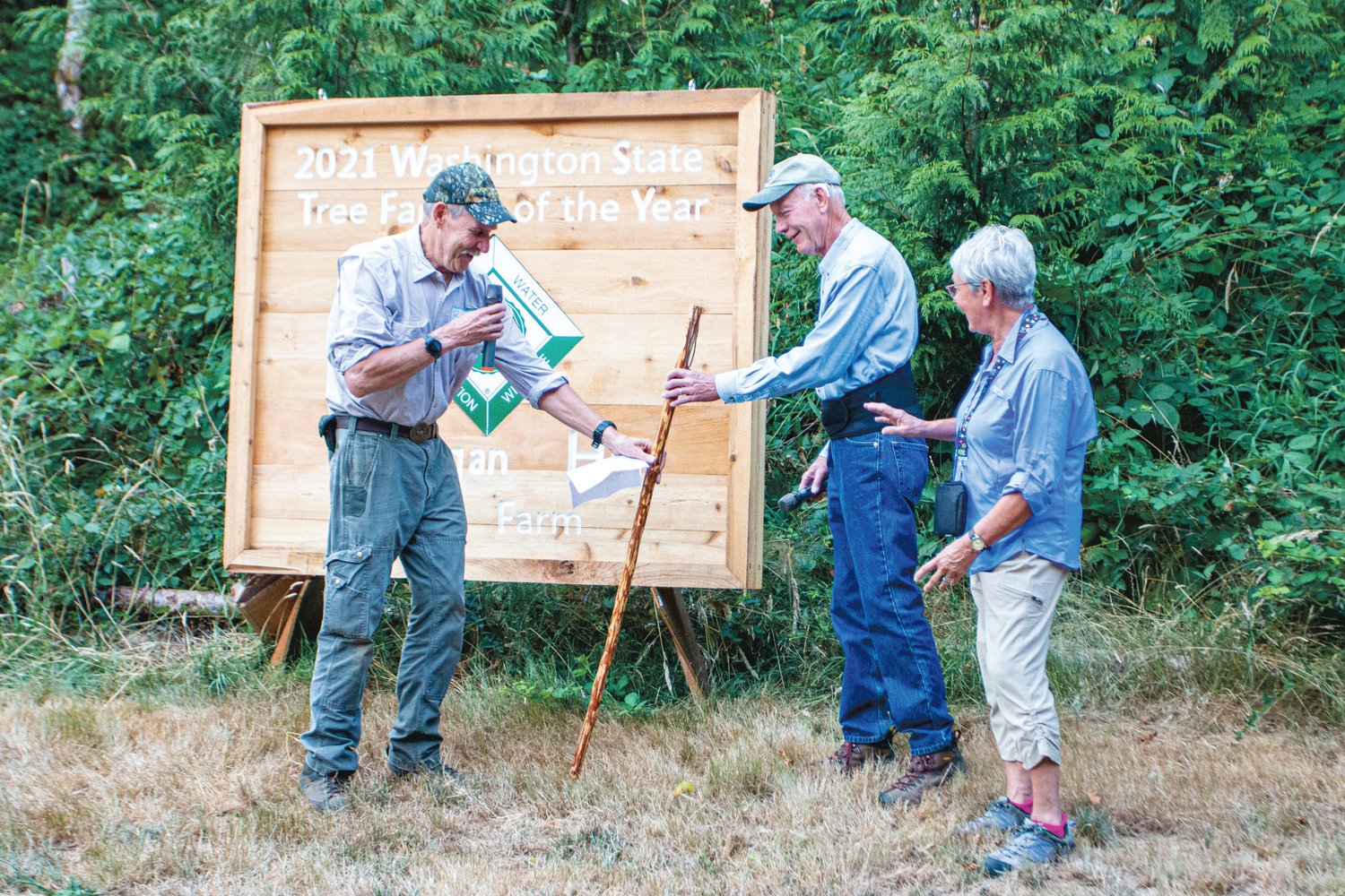 Bob Obideski, chair of the Washington Tree Farm Program, hands a staff to Chuck Higgins and Nan Reber Higgins, the 2021 Washington State Tree Farmers of the Year.